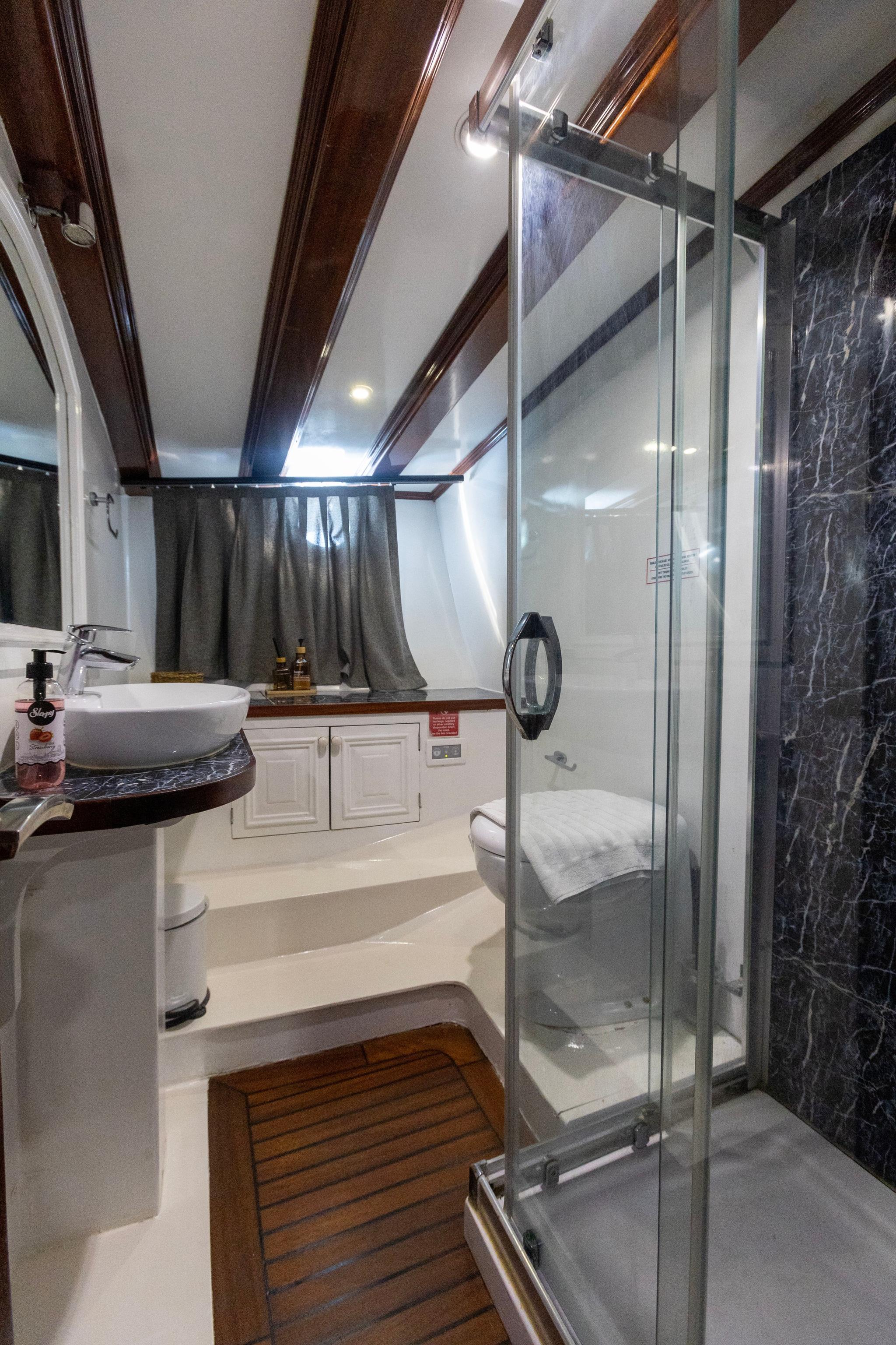 luxury yacht bathroom featuring glass shower enclosure, white vessel sink, and dark marble walls