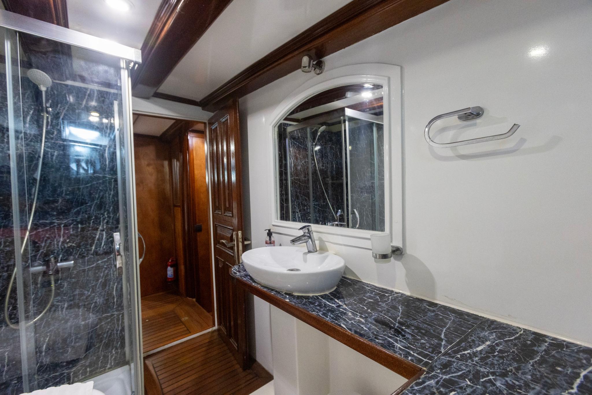 yacht bathroom featuring marble shower enclosure, round white basin, and wooden cabinetry
