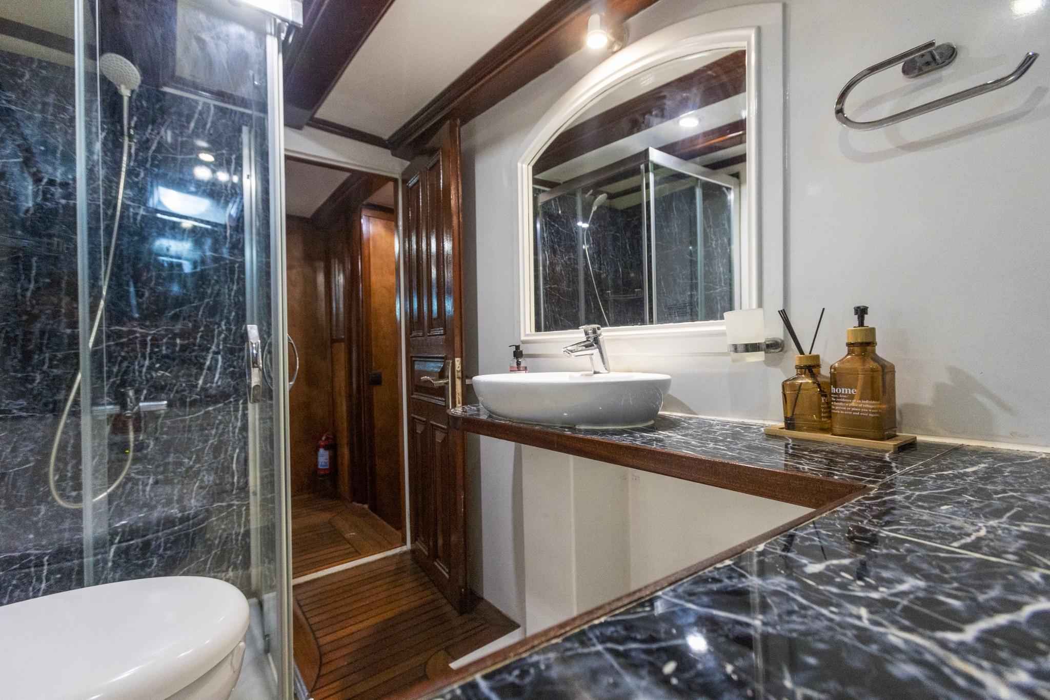 yacht bathroom featuring white vessel sink on marble countertop with glass shower enclosure