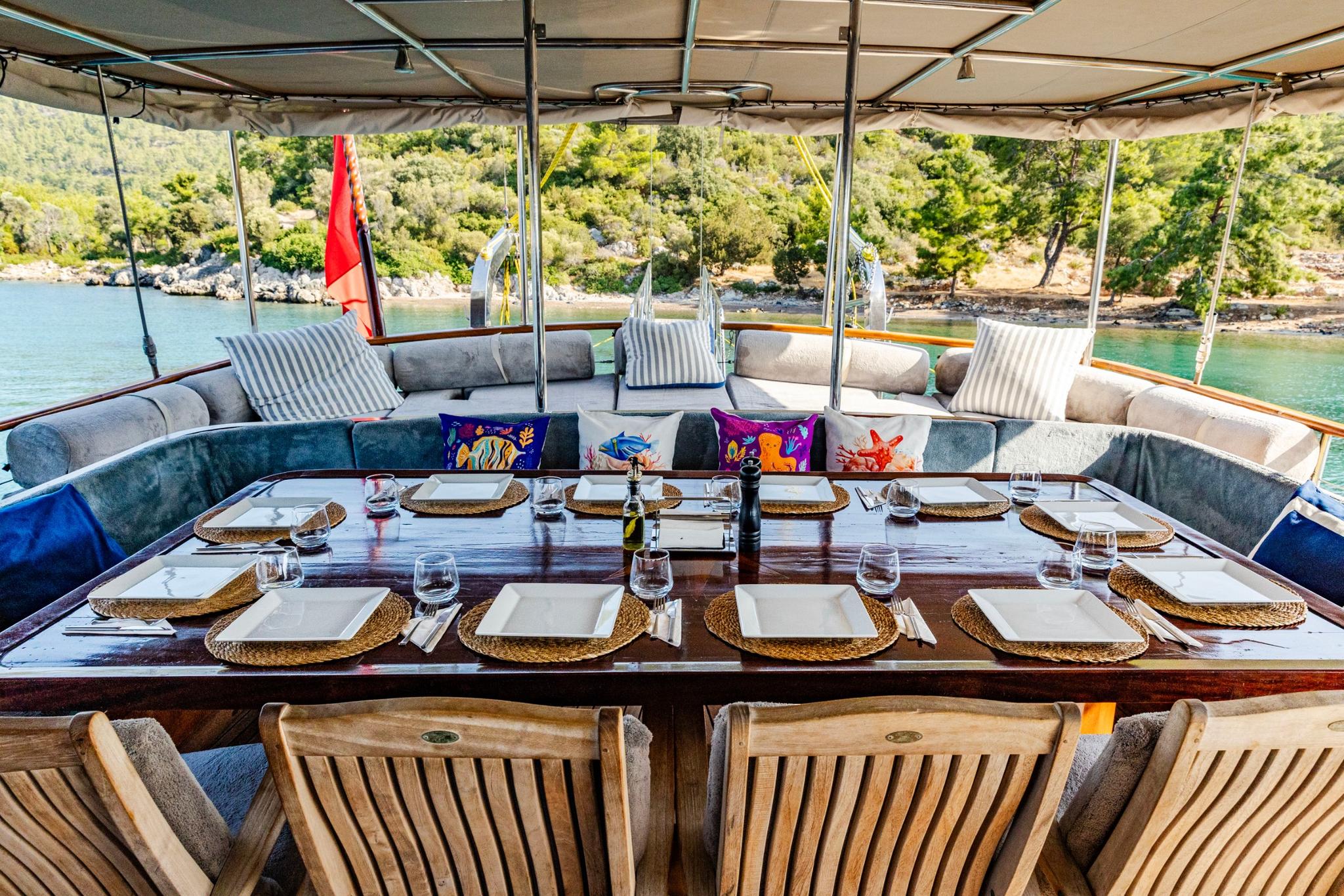 aft deck dining table with woven placemats, wine glasses and cushioned seating area