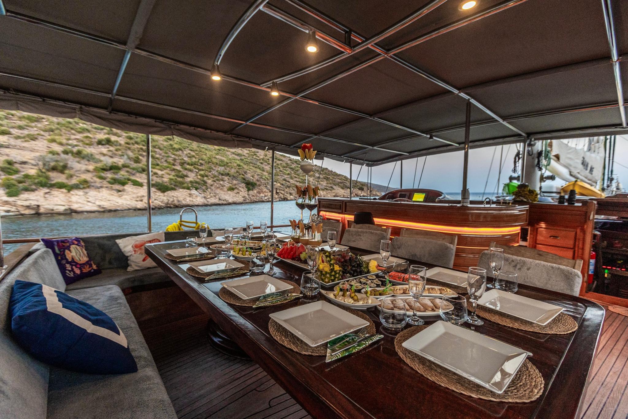 gulet aft deck dining table set with served food dishes and wine glasses