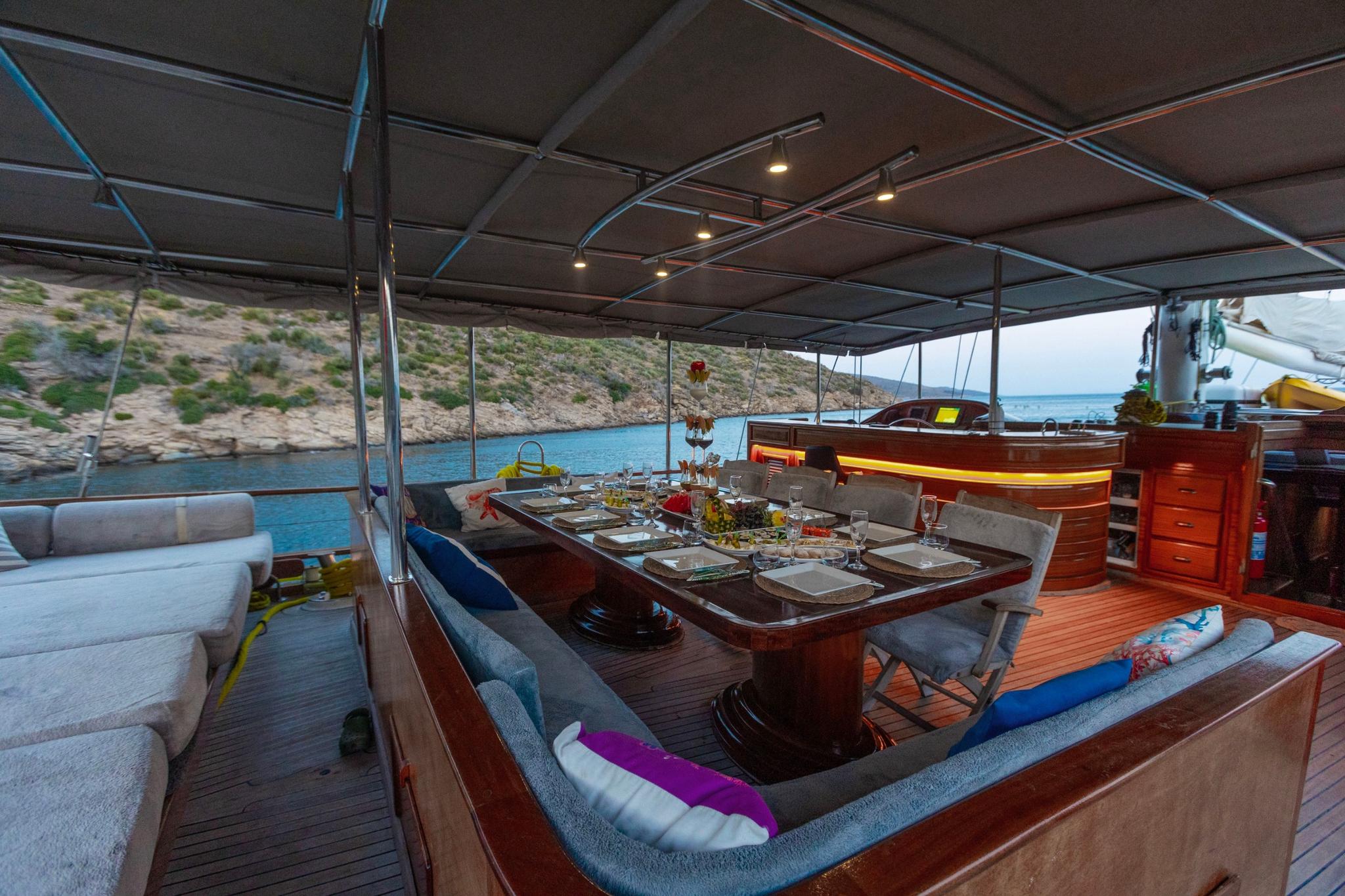 gulet aft deck with outdoor dining table, cushioned seating, and partial canopy coverage