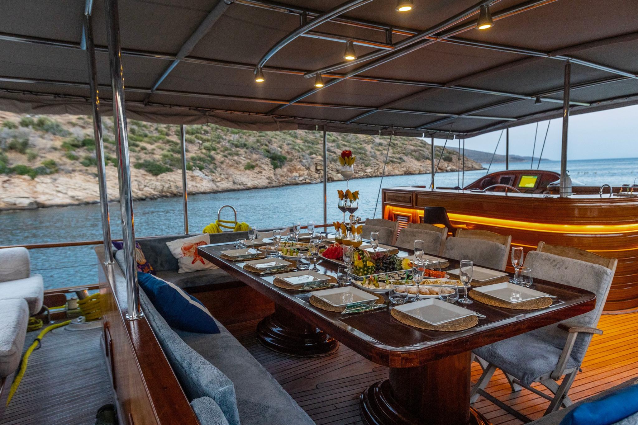 Aft deck dining area with set table, food platters, wine glasses and coastal backdrop