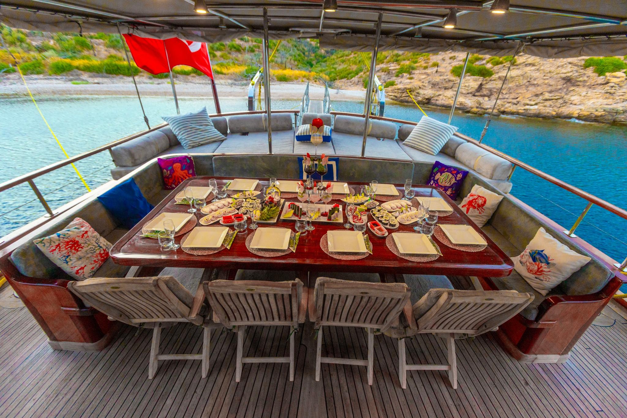 outdoor dining area with formal table setting, served food platters and wine glasses on gulet