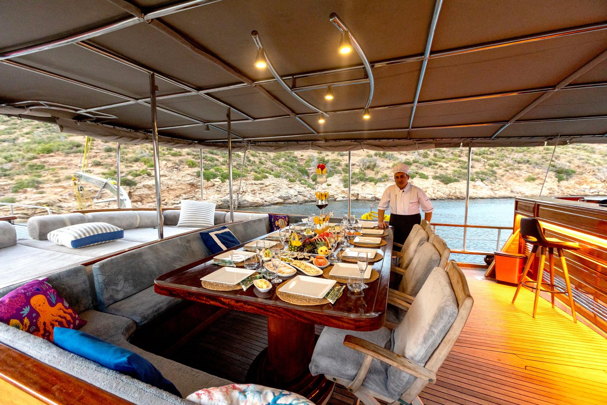 crew member in white uniform serving formal dinner on yacht's covered aft dining area