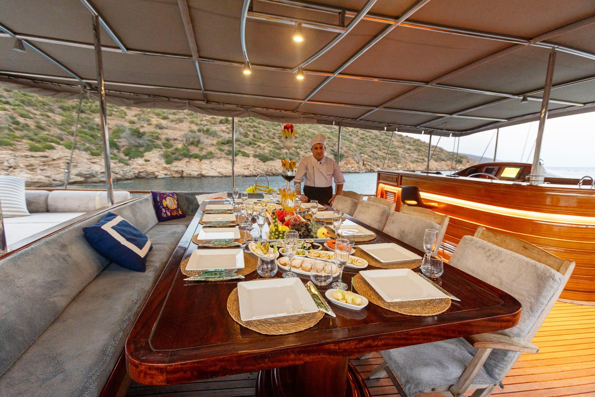formal dining table with place settings and crew member serving guests on yacht aft deck