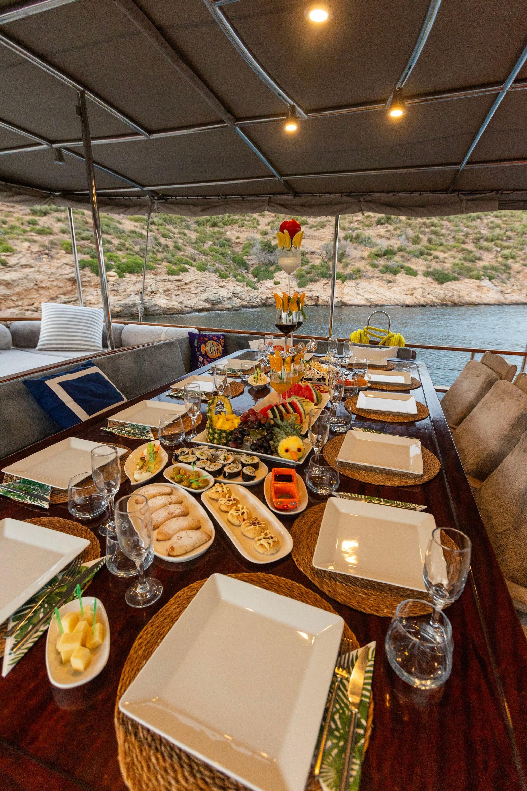 yacht dining table with elaborate appetizer spread, wine glasses and place settings under awning