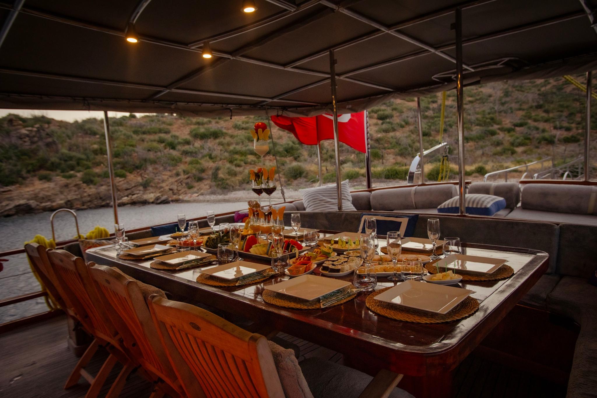 aft deck dining table set with food plates, wine glasses and appetizers at sunset