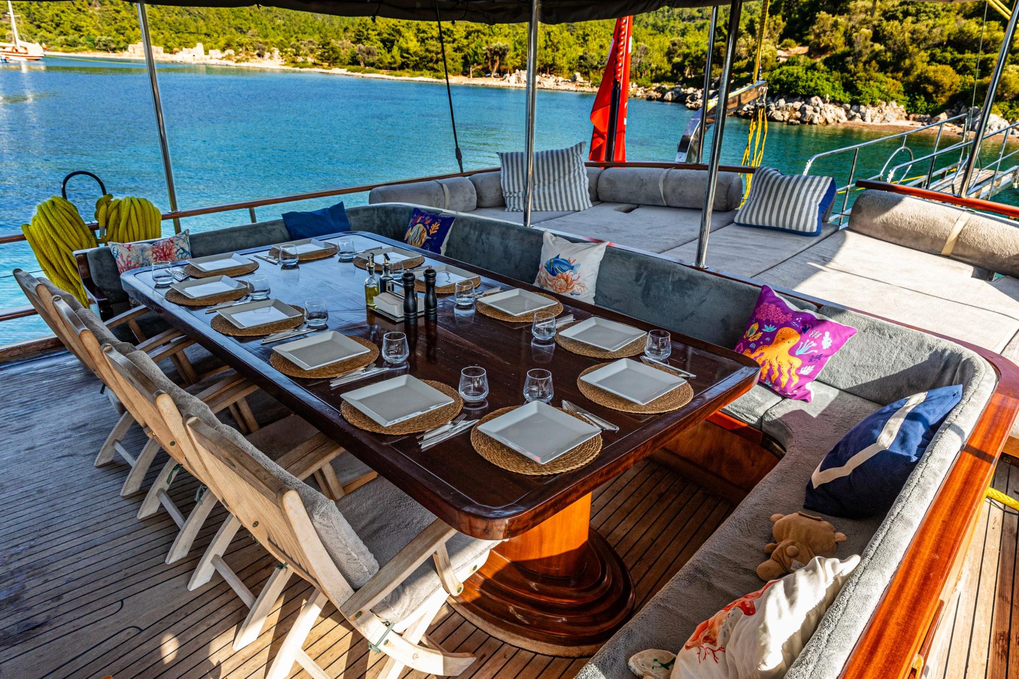 Gulet aft deck with formal dining table, built-in seating and scenic bay view