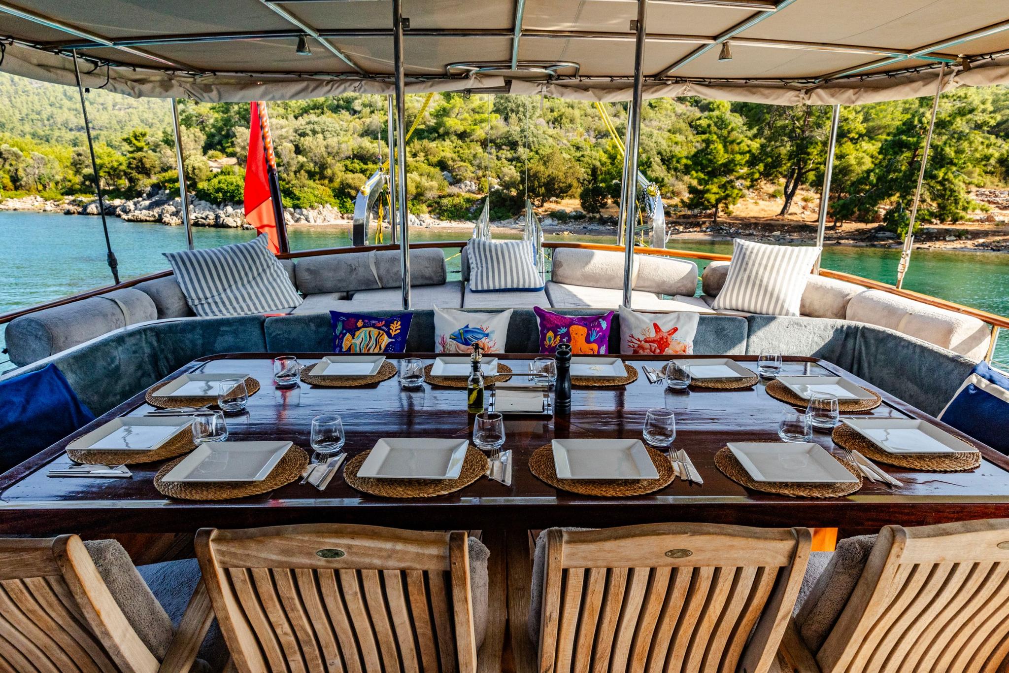 aft deck dining table with wicker placemats, wine glasses and cushioned seating area