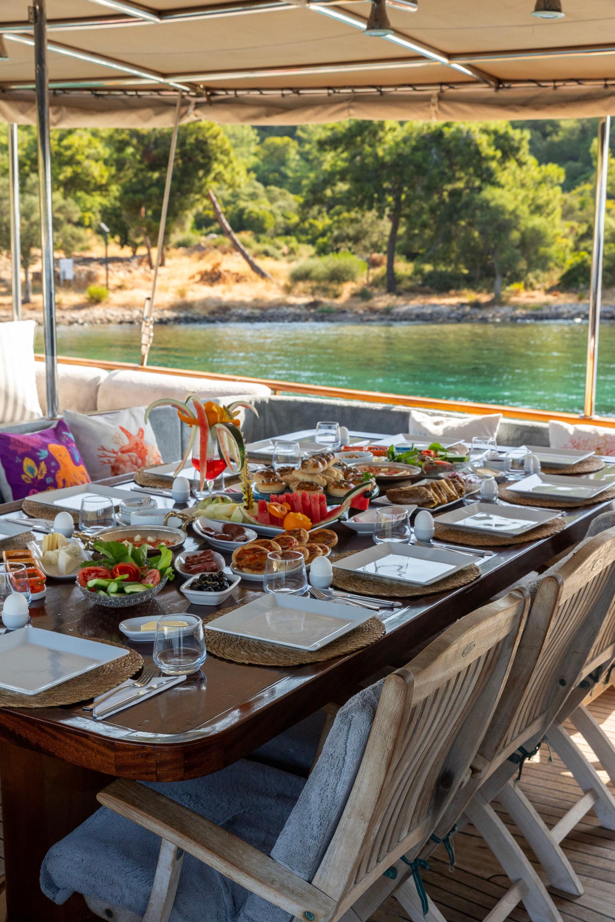 Yacht aft deck dining table with elaborate breakfast spread including pastries, fruits, and table settings