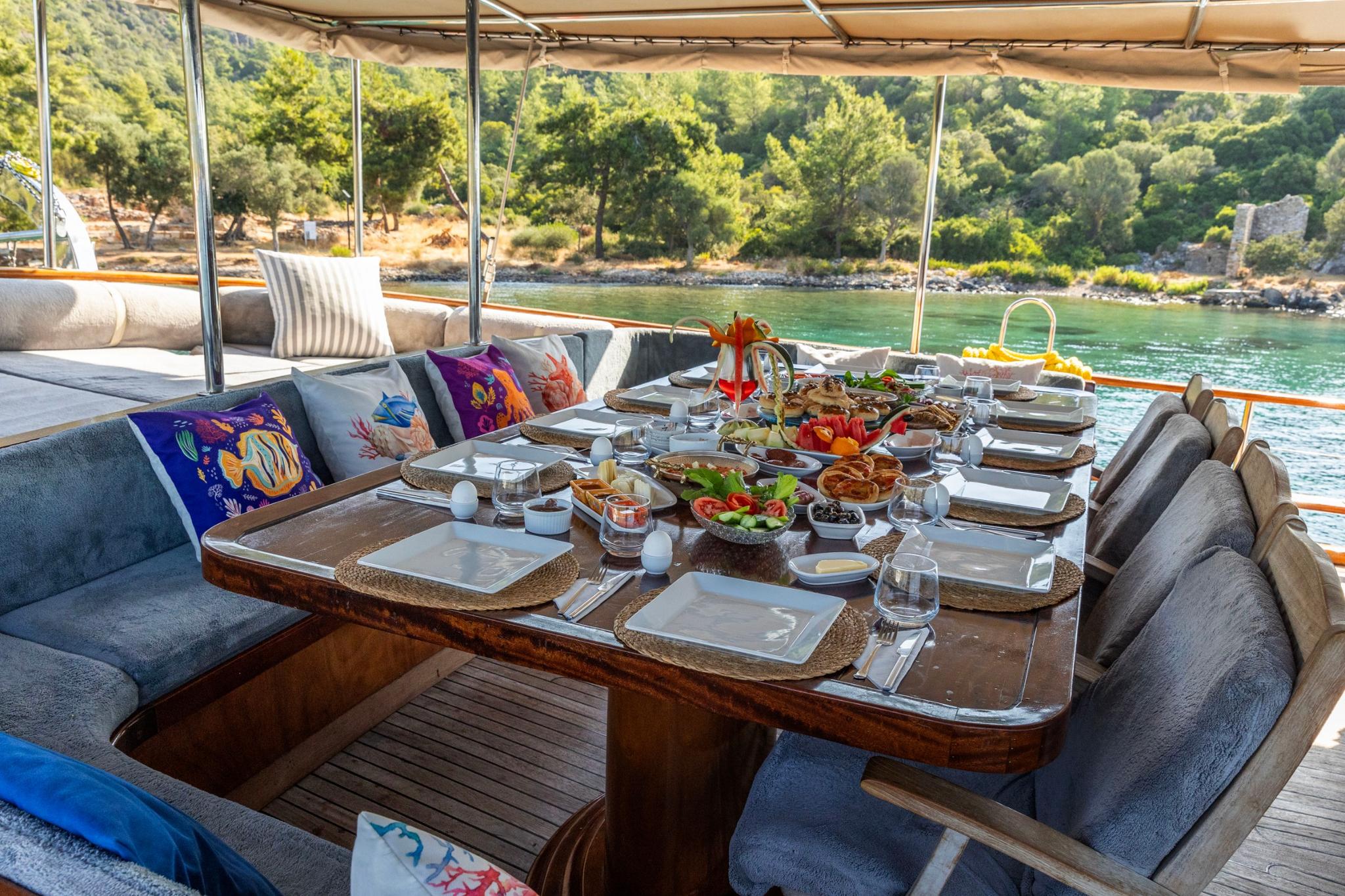 Outdoor dining table with elaborate Turkish breakfast spread featuring colorful cushions and bay view