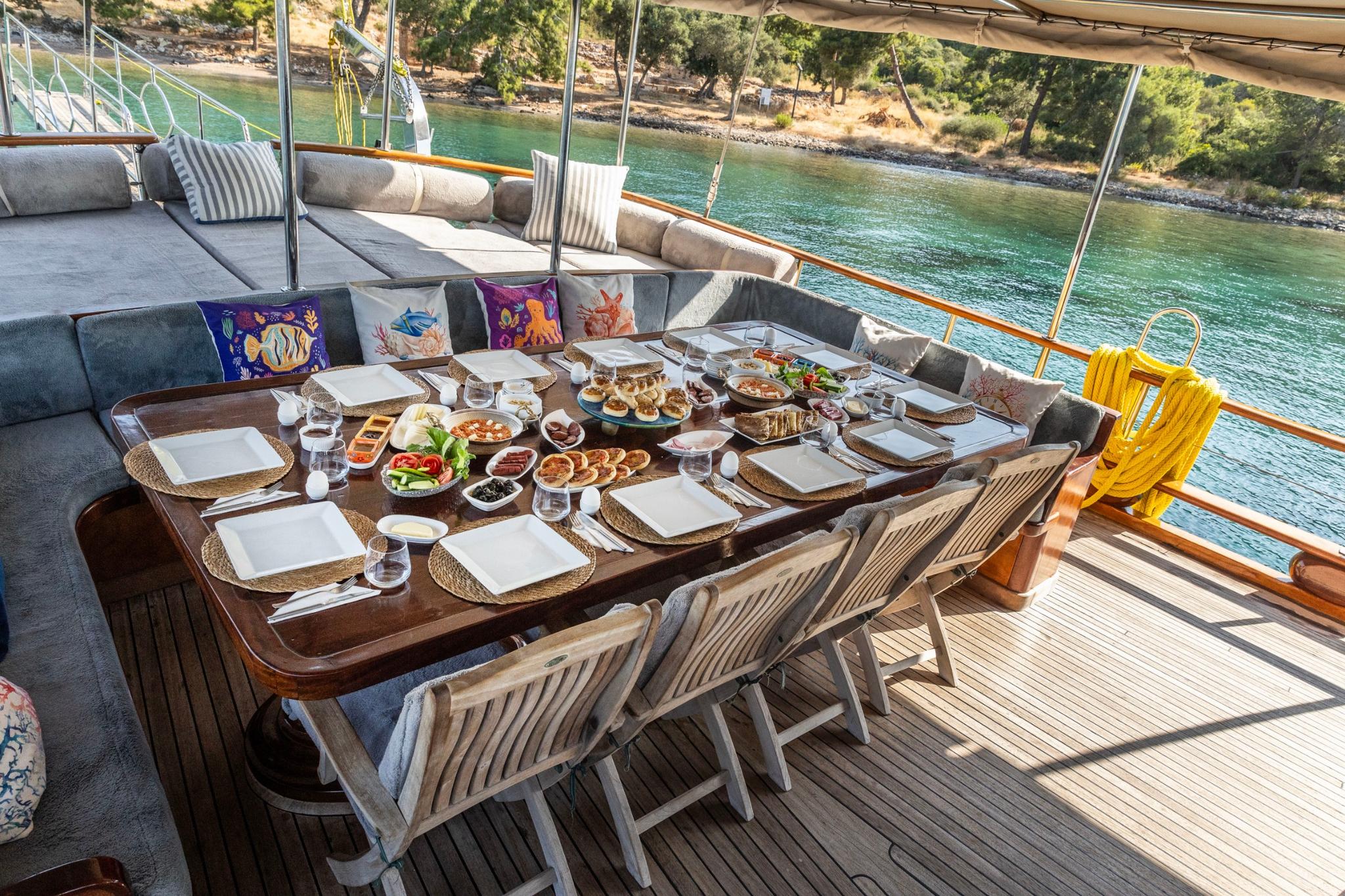 yacht aft deck dining table set with breakfast spread overlooking turquoise bay