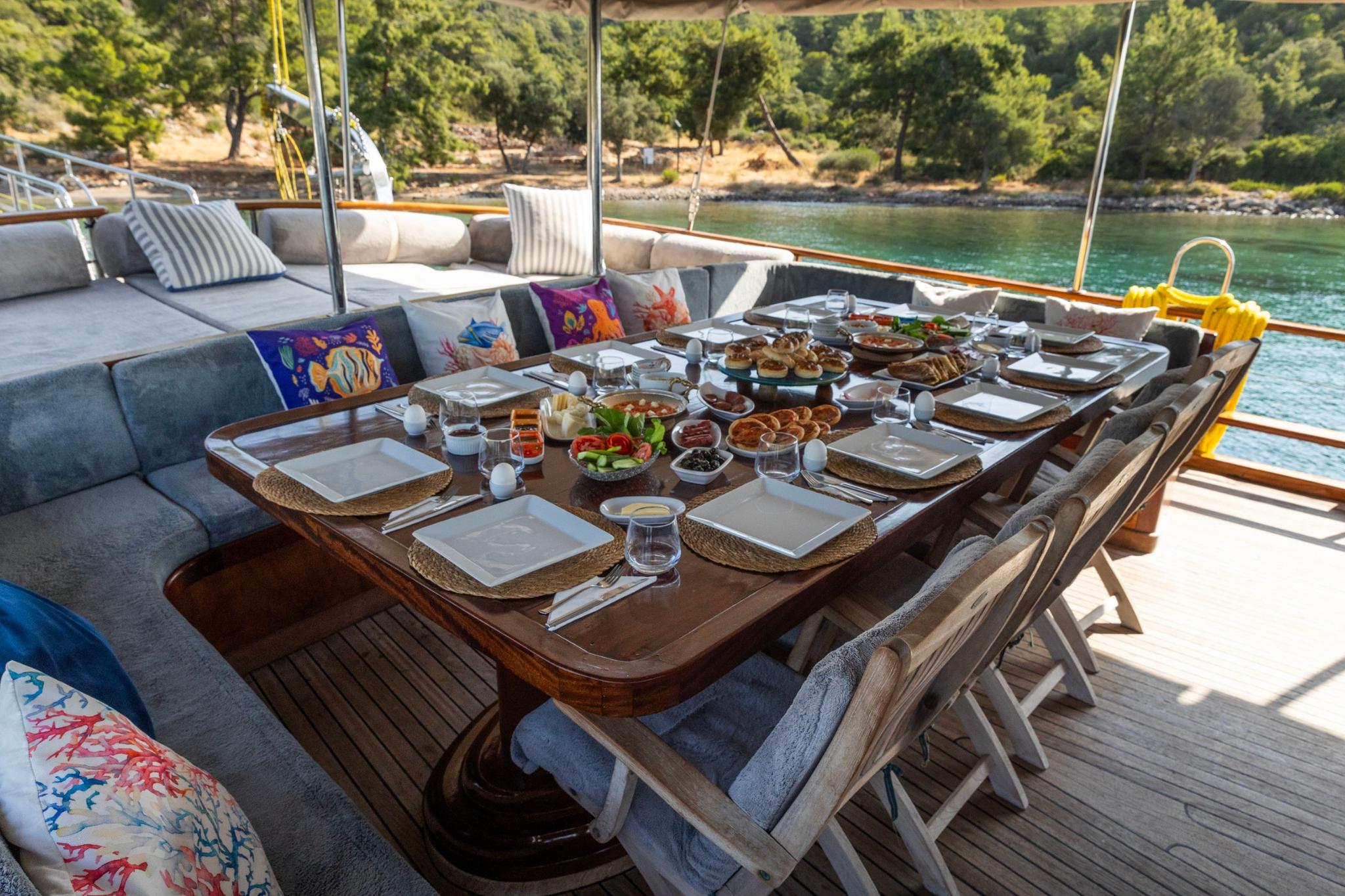 outdoor breakfast table set with food spread, plates and glasses on gulet deck