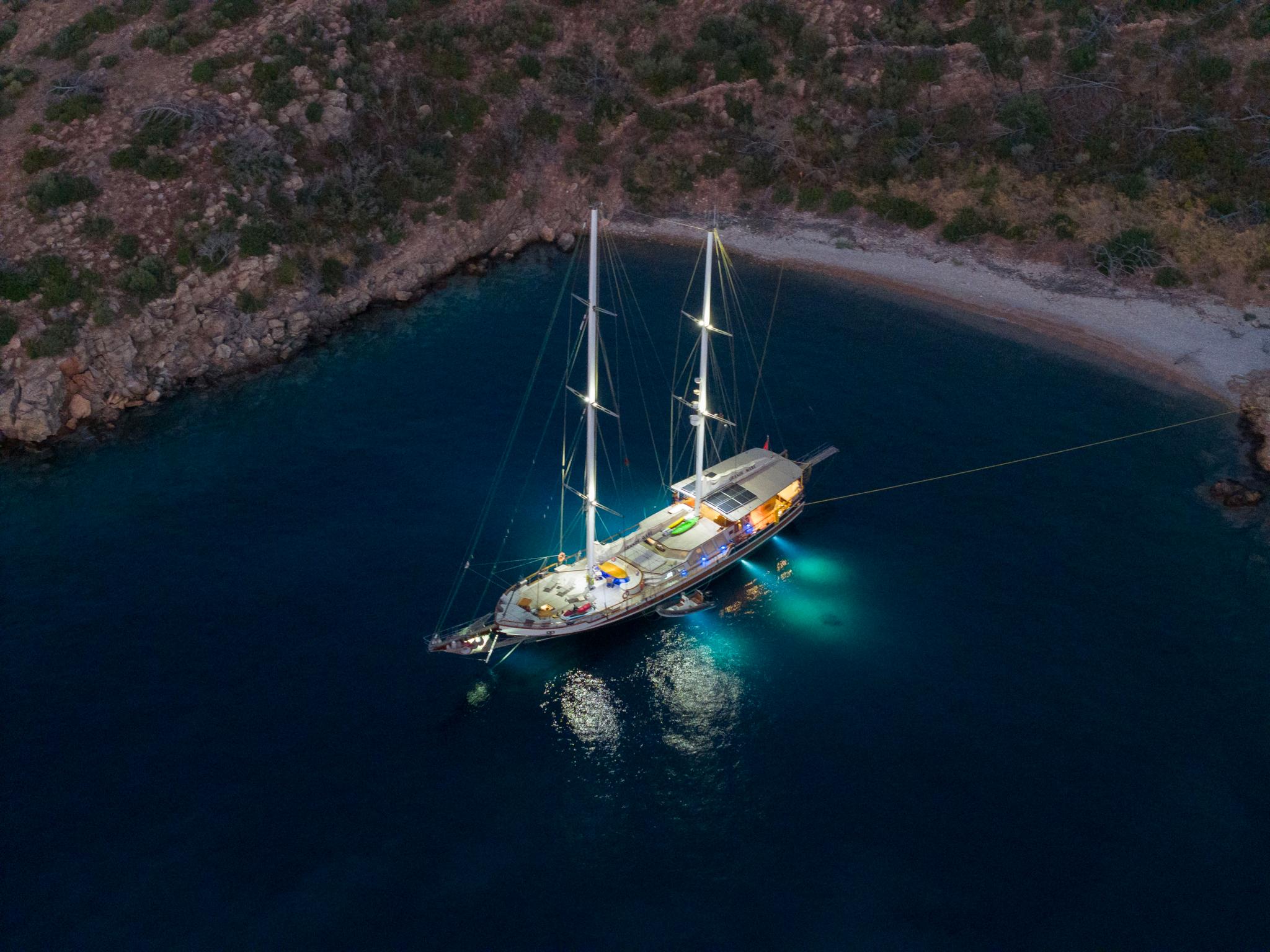aerial view of traditional gulet yacht anchored in protected bay with underwater lighting at twilight