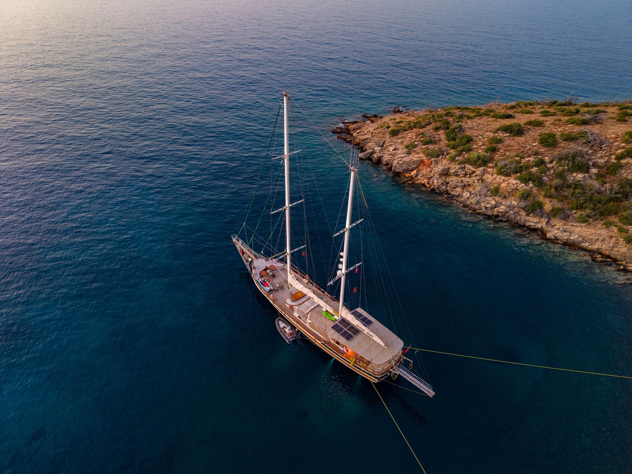 aerial view of traditional wooden gulet with two masts anchored in turquoise waters near rocky coast