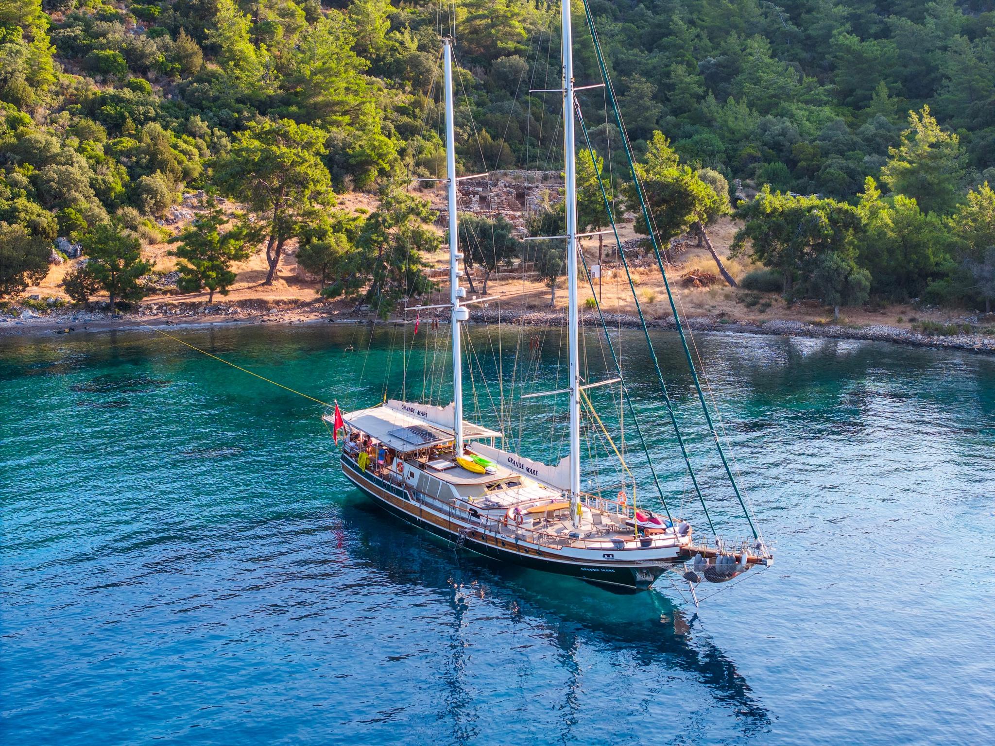 Traditional wooden gulet yacht at anchor in crystal clear turquoise waters near forested coastline