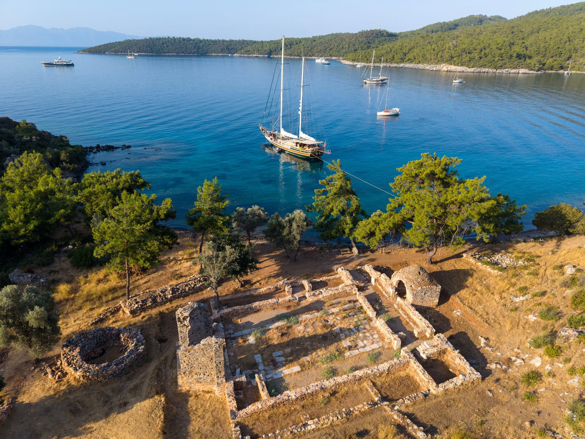 aerial view of traditional gulet yacht anchored in turquoise Mediterranean bay with ancient stone ruins in foreground