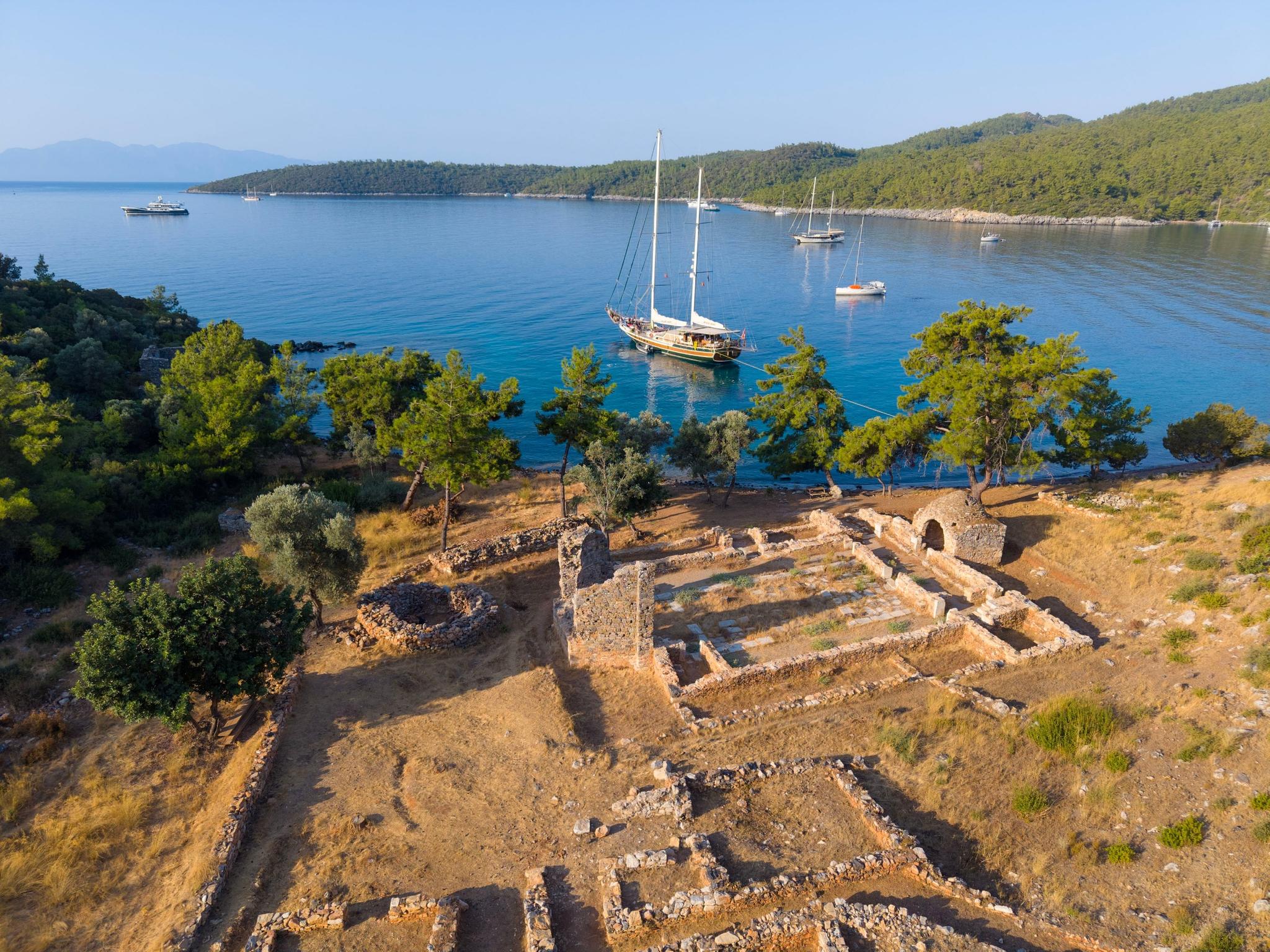 aerial view of traditional wooden gulet yacht anchored in turquoise bay near ancient stone ruins