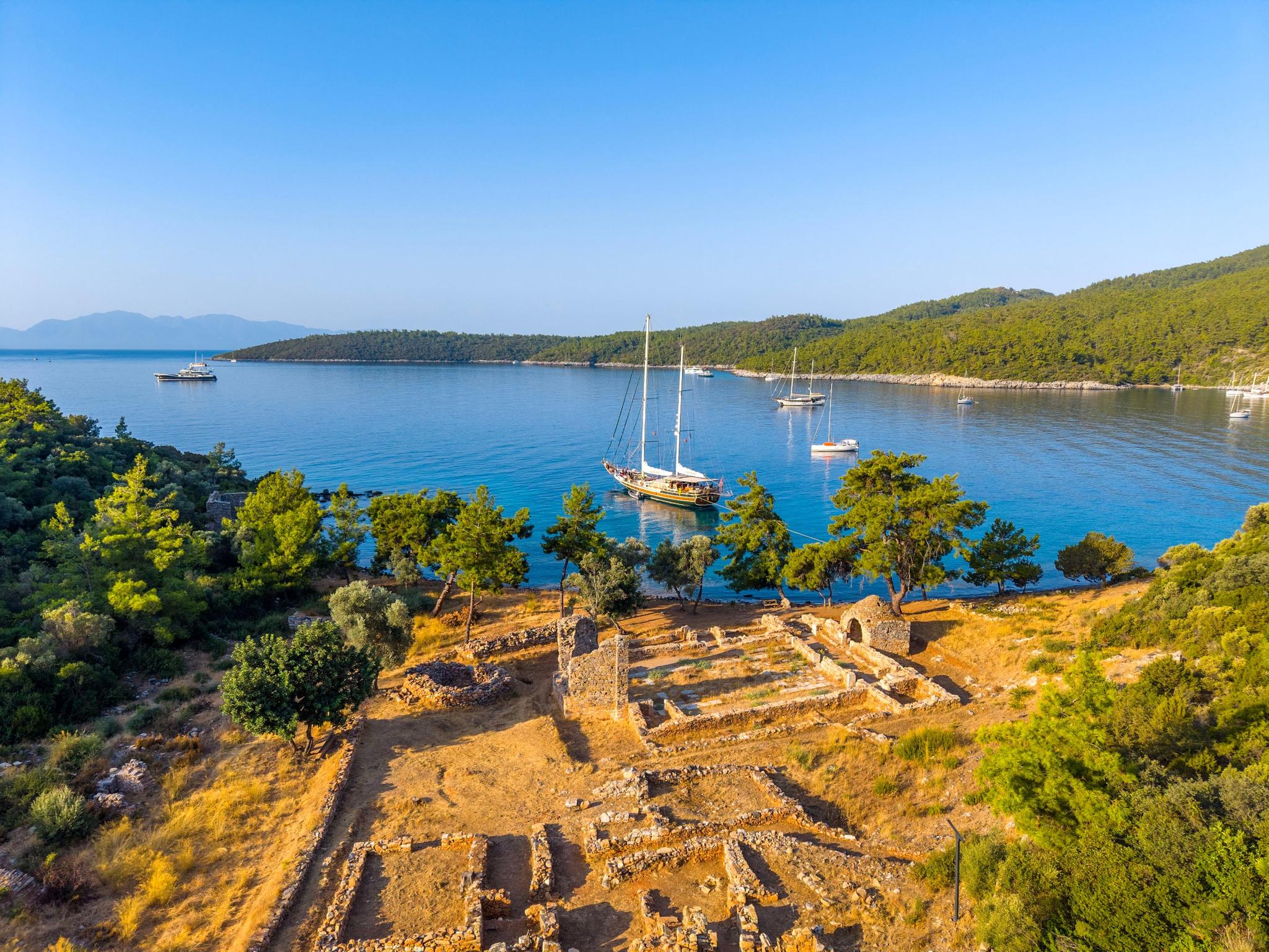aerial view of traditional gulet yacht anchored in turquoise bay near ancient stone ruins