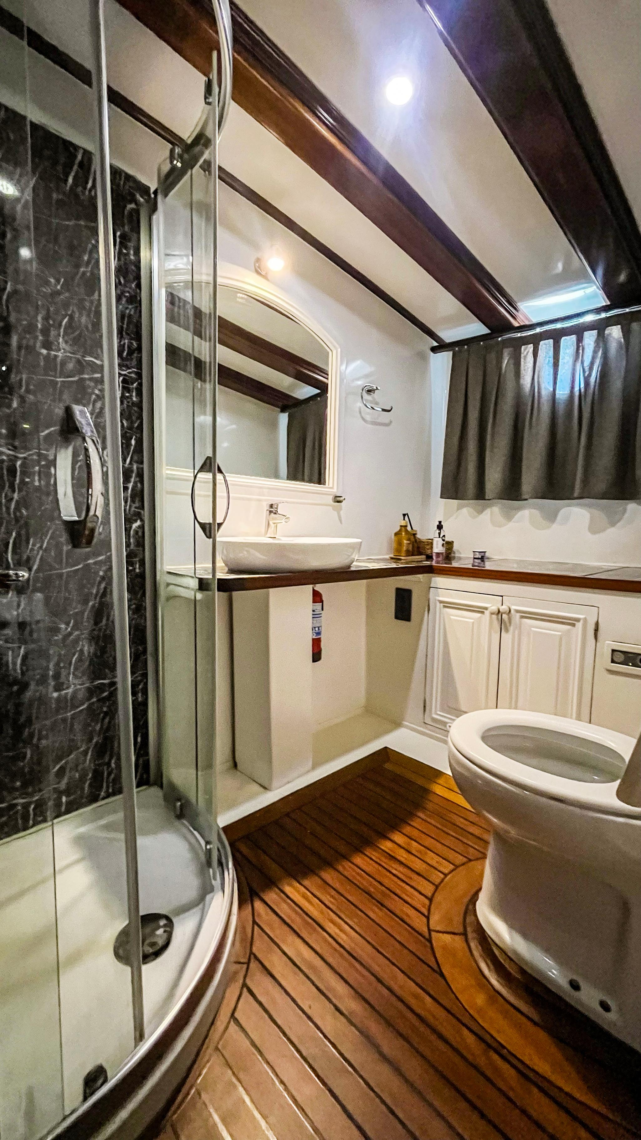 compact yacht bathroom featuring glass shower enclosure, toilet, vessel sink and teak flooring