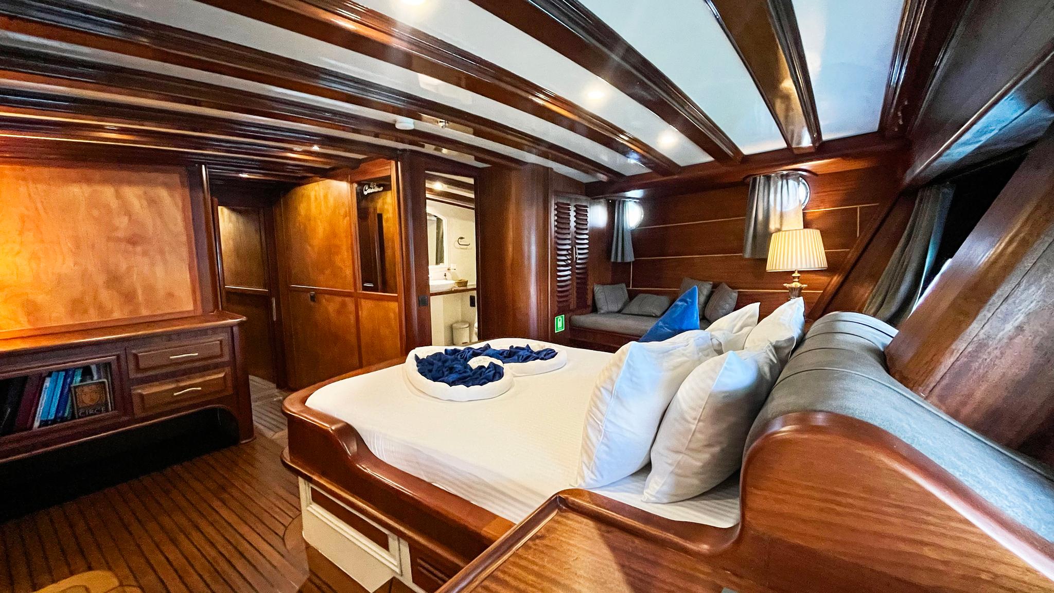 luxury yacht master cabin featuring double bed with white linens, rich wood paneling, and en-suite bathroom entrance