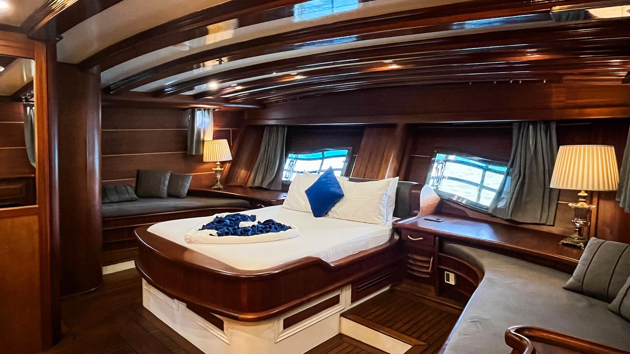 Luxury yacht master cabin featuring king bed with white linens, dark wood paneling, and twin portholes