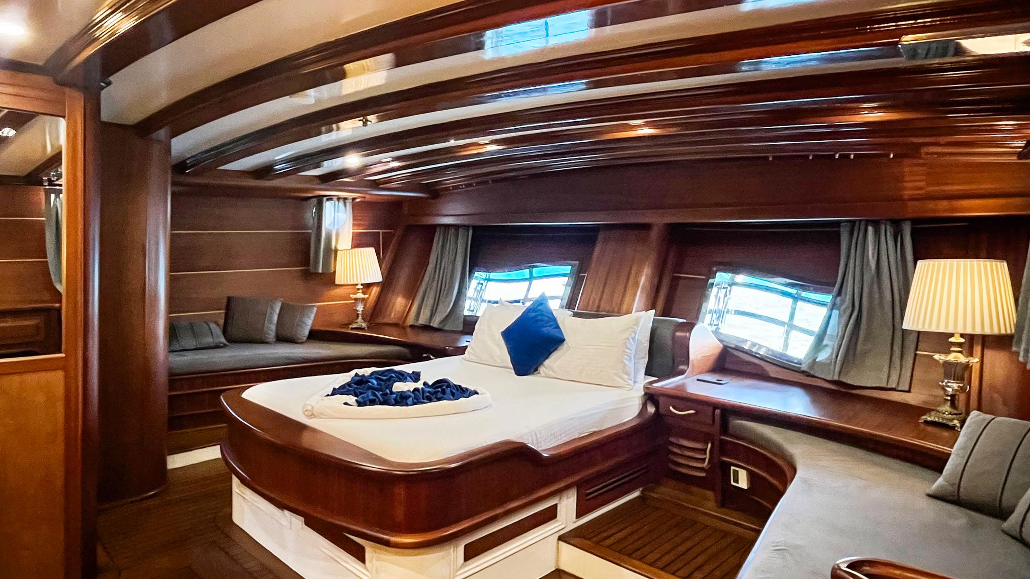 yacht cabin interior with curved bed, grey cushioned seating, portholes and wooden paneling
