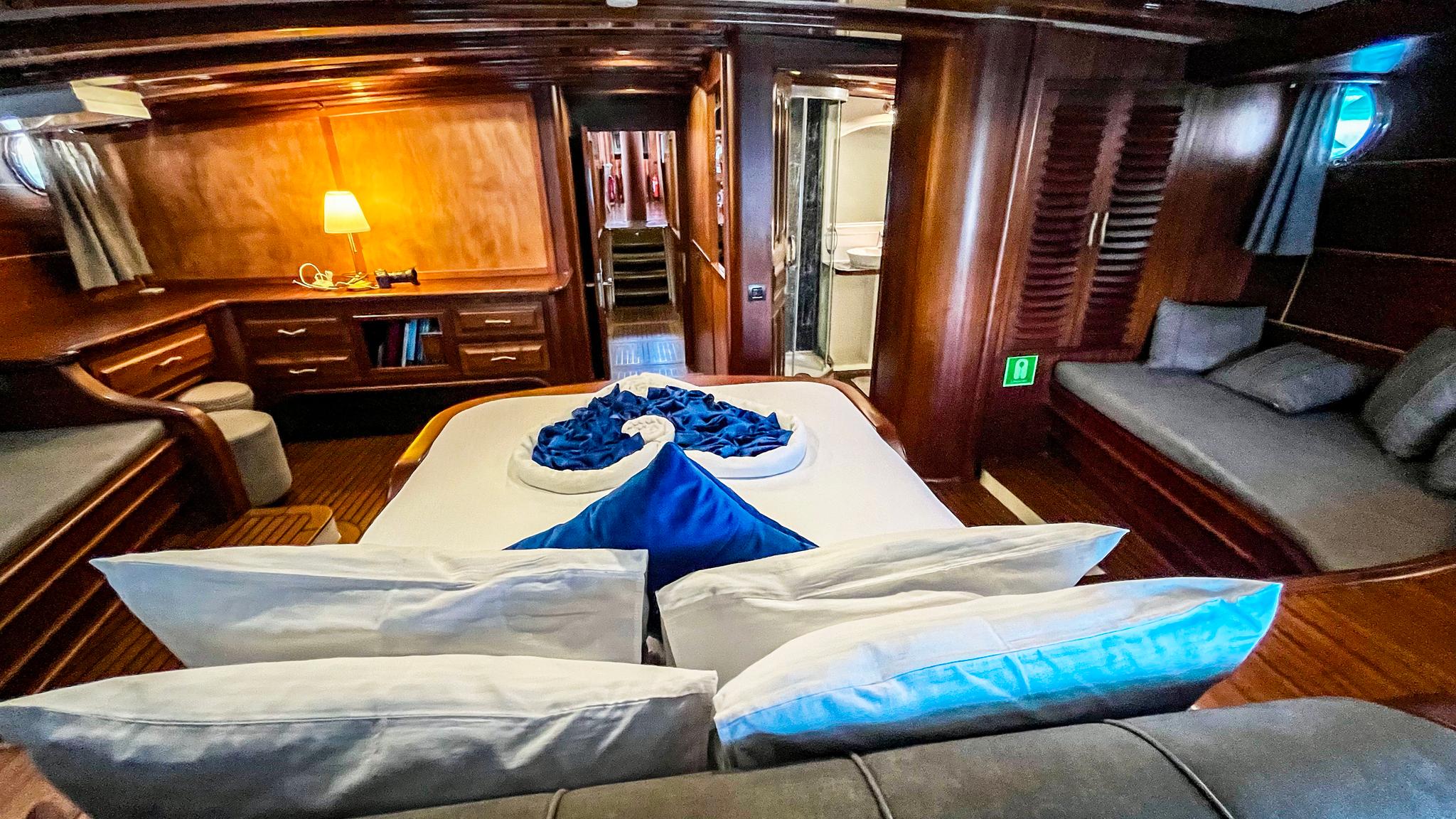 yacht cabin interior with double bed, blue towel swan decoration, built-in seating and wooden paneling
