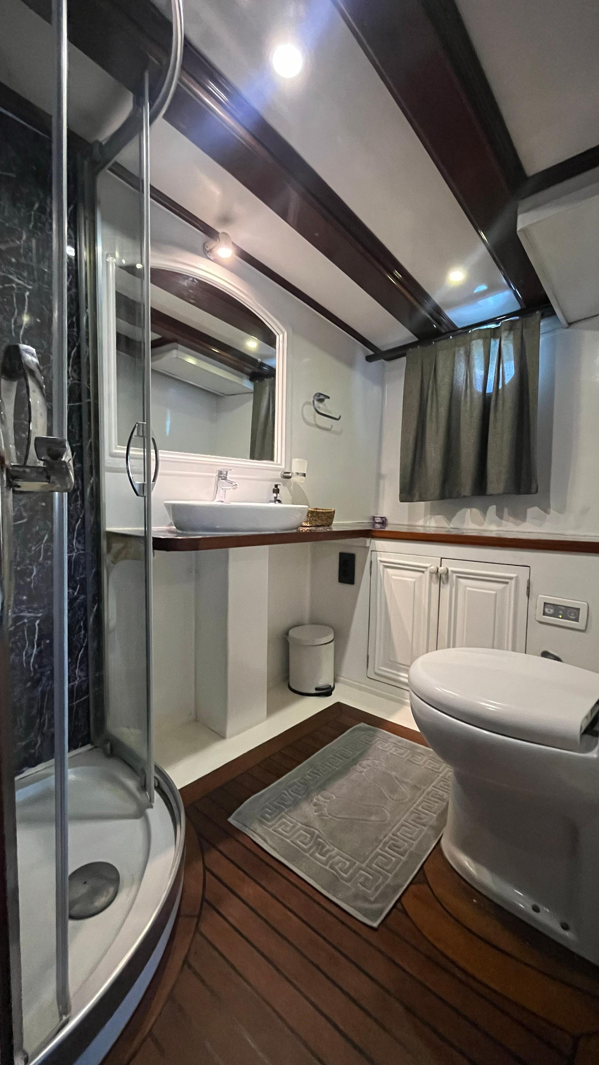 luxury yacht en-suite bathroom with glass shower enclosure, vessel sink and teak wood flooring