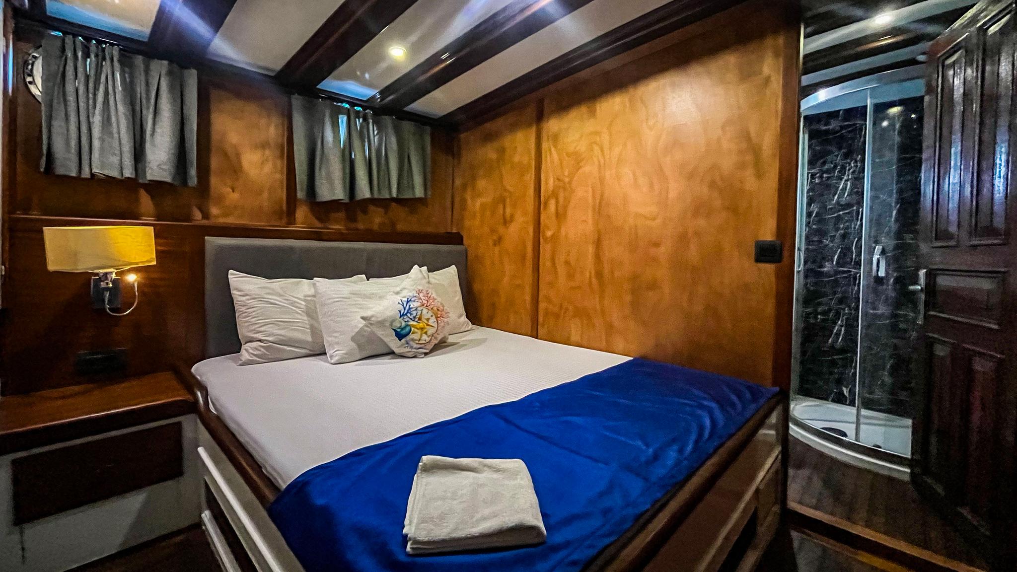 yacht guest cabin featuring double bed with blue throw, wooden paneling and marble shower enclosure