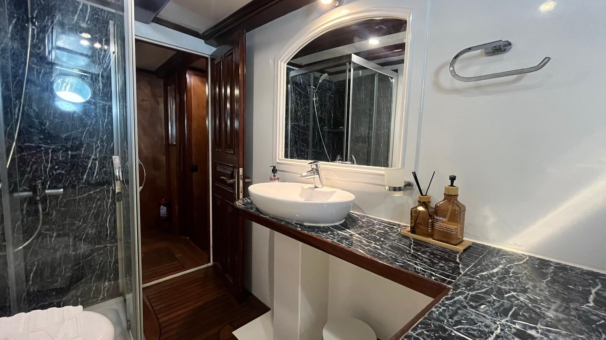 luxury yacht bathroom featuring dark marble walls, white vessel sink, and glass shower enclosure