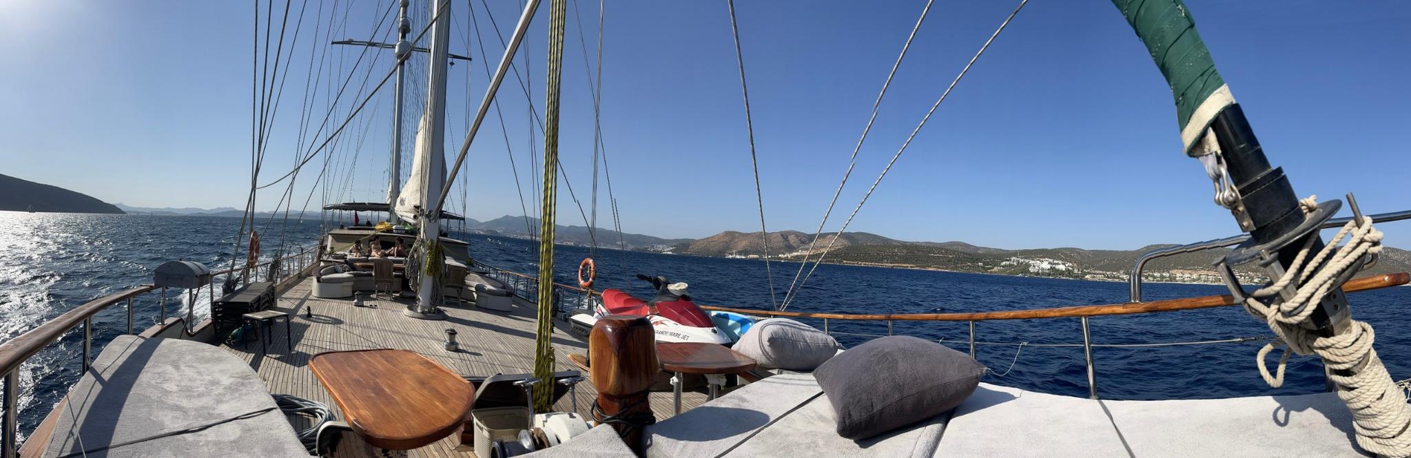 gulet sailing deck with rigging, masts, and Mediterranean coastline in background