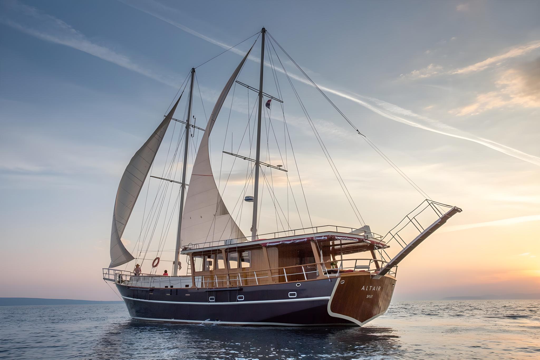Traditional wooden gulet yacht Altair under sail with blue hull and white sails at sunset