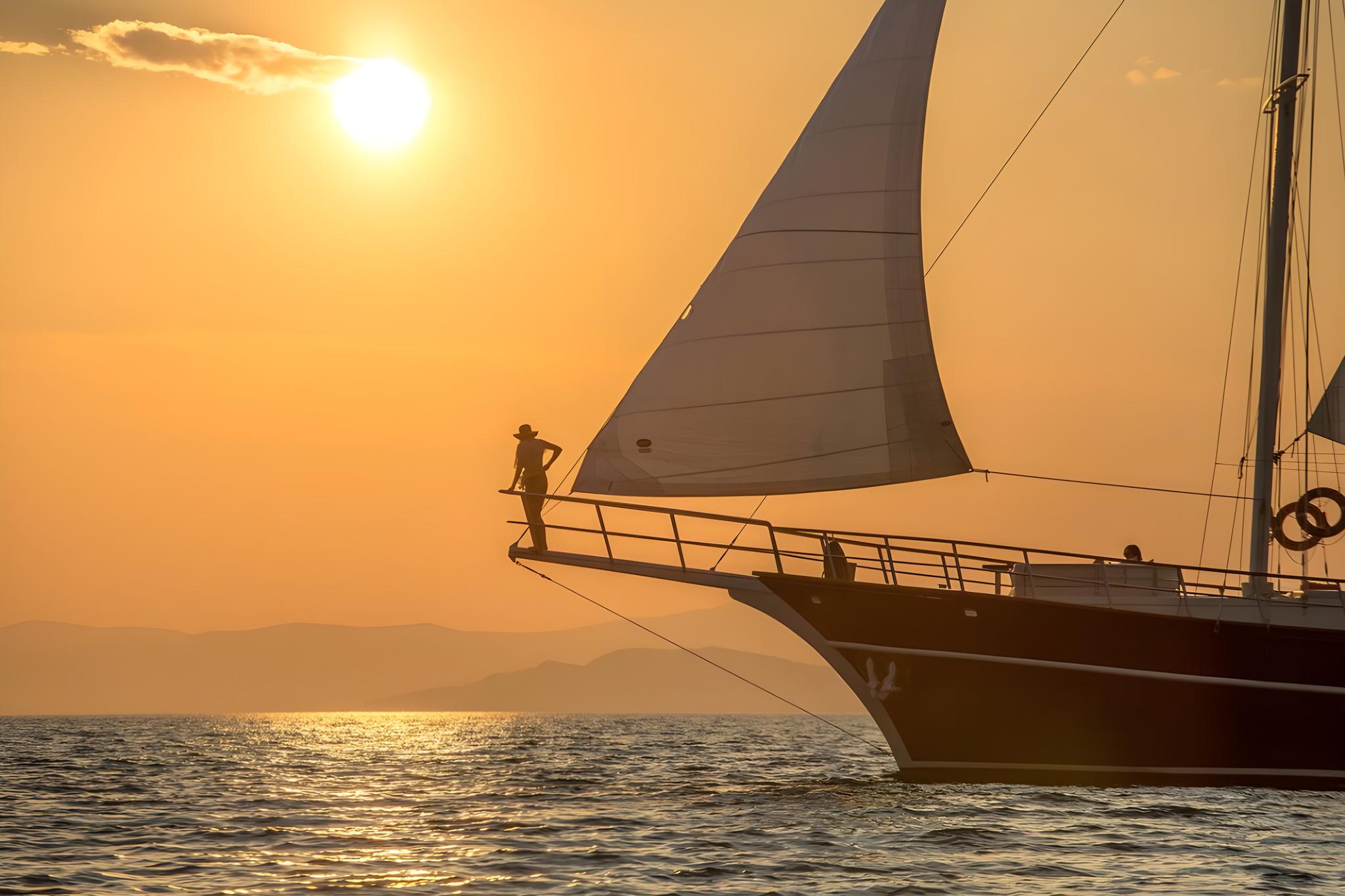 Traditional wooden gulet yacht sailing at sunset with crew member silhouetted on bow deck