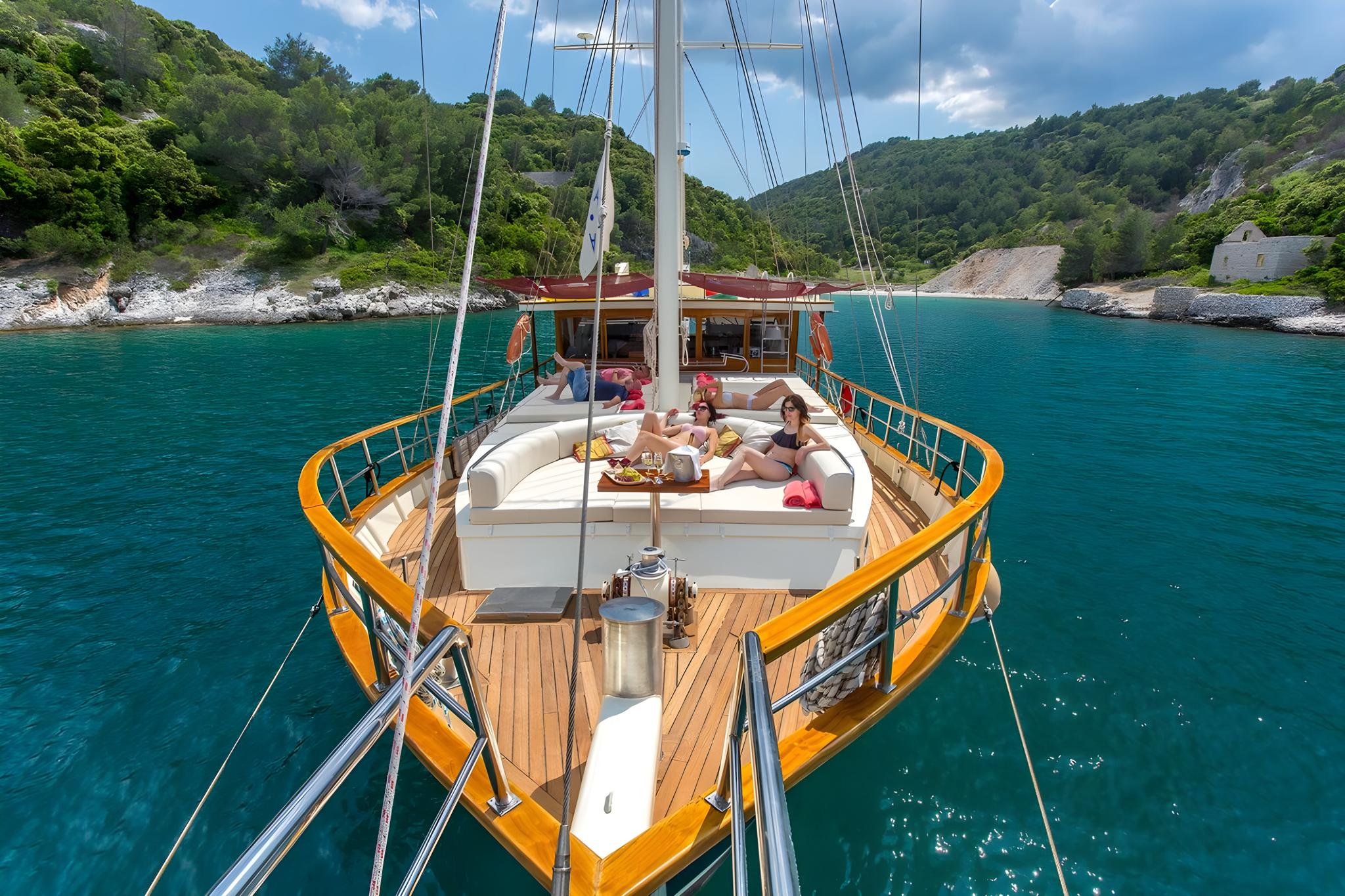 Gulet bow deck with white cushioned seating area and guests lounging in turquoise bay