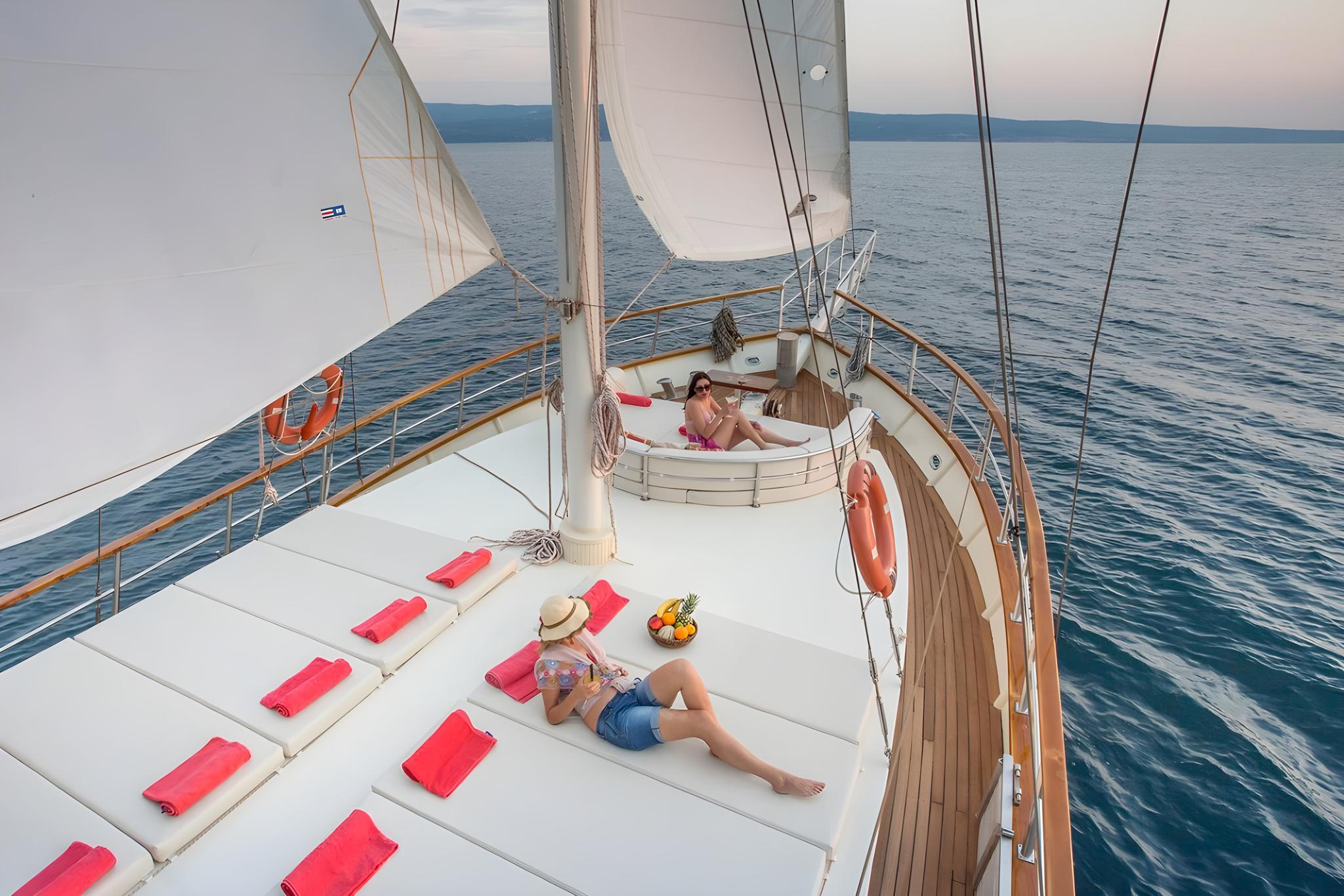 sailing yacht forward sun deck with curved seating area and guests relaxing under white sails