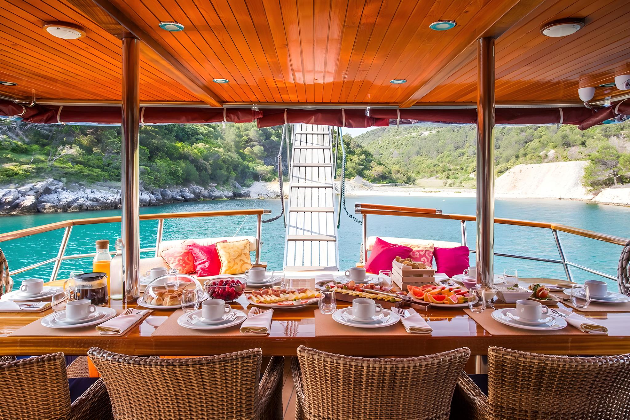 yacht dining table set with breakfast spread, coffee cups, and Mediterranean bay view