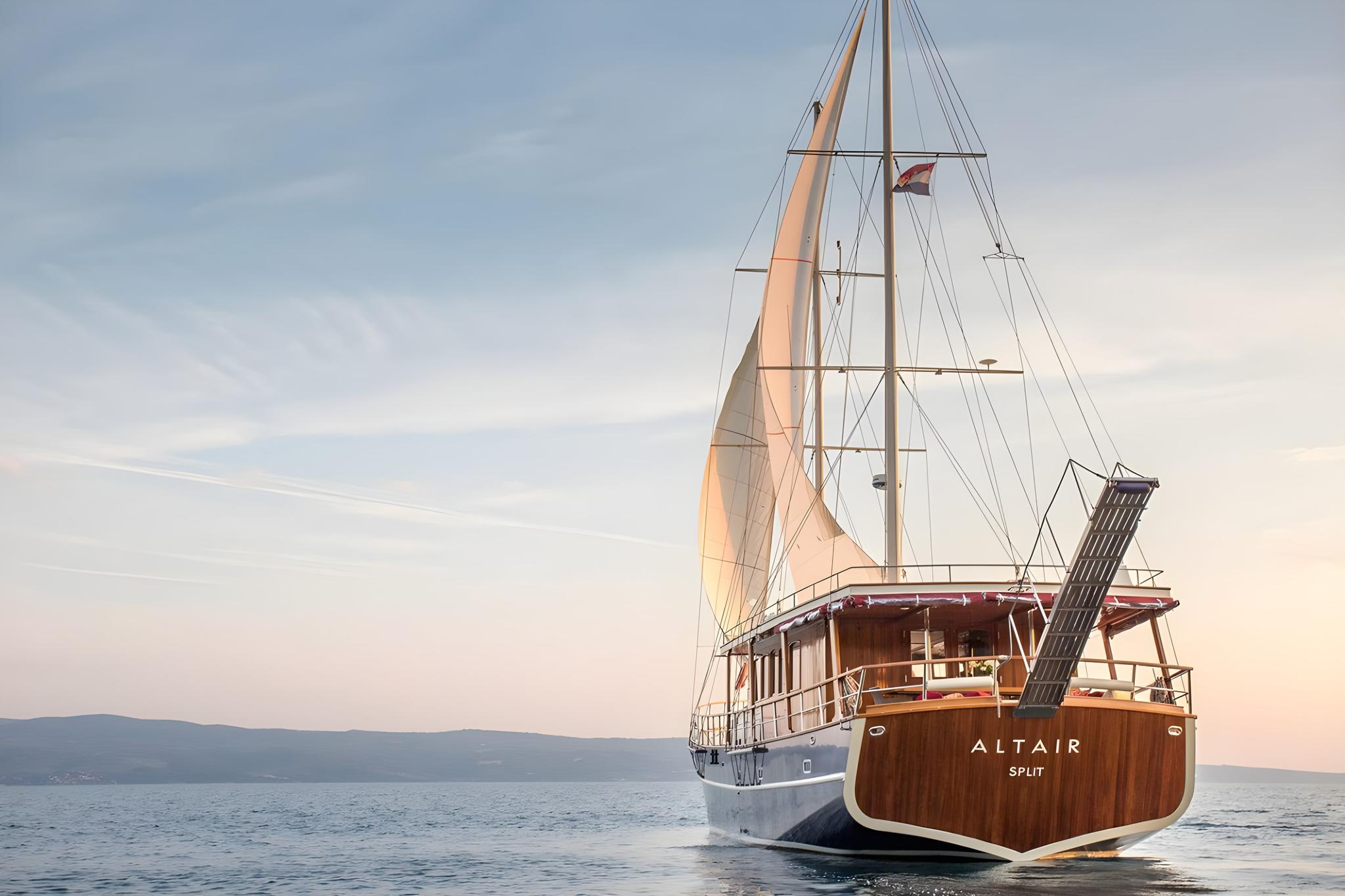 Traditional wooden gulet Altair under sail on calm waters at sunset with mountain coastline