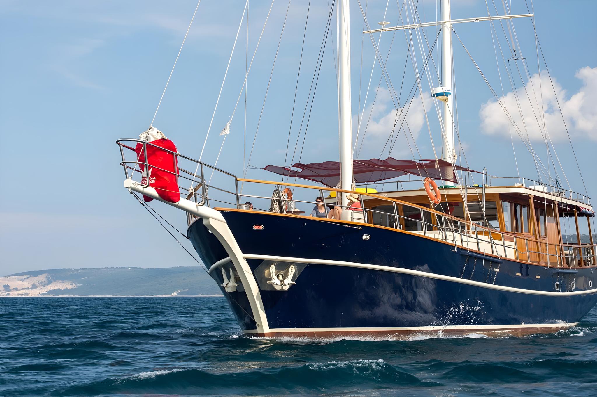 Traditional wooden gulet with dark blue hull and burgundy sails sailing on open water