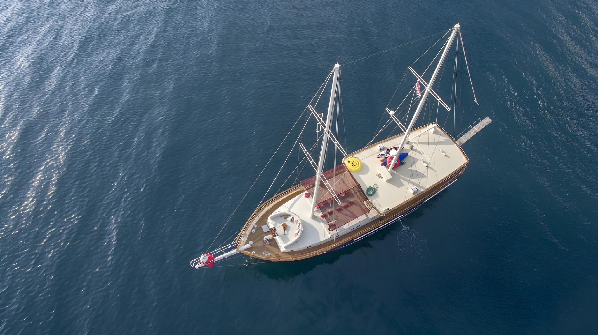 aerial drone shot of traditional wooden gulet yacht with two masts anchored in deep blue Mediterranean waters