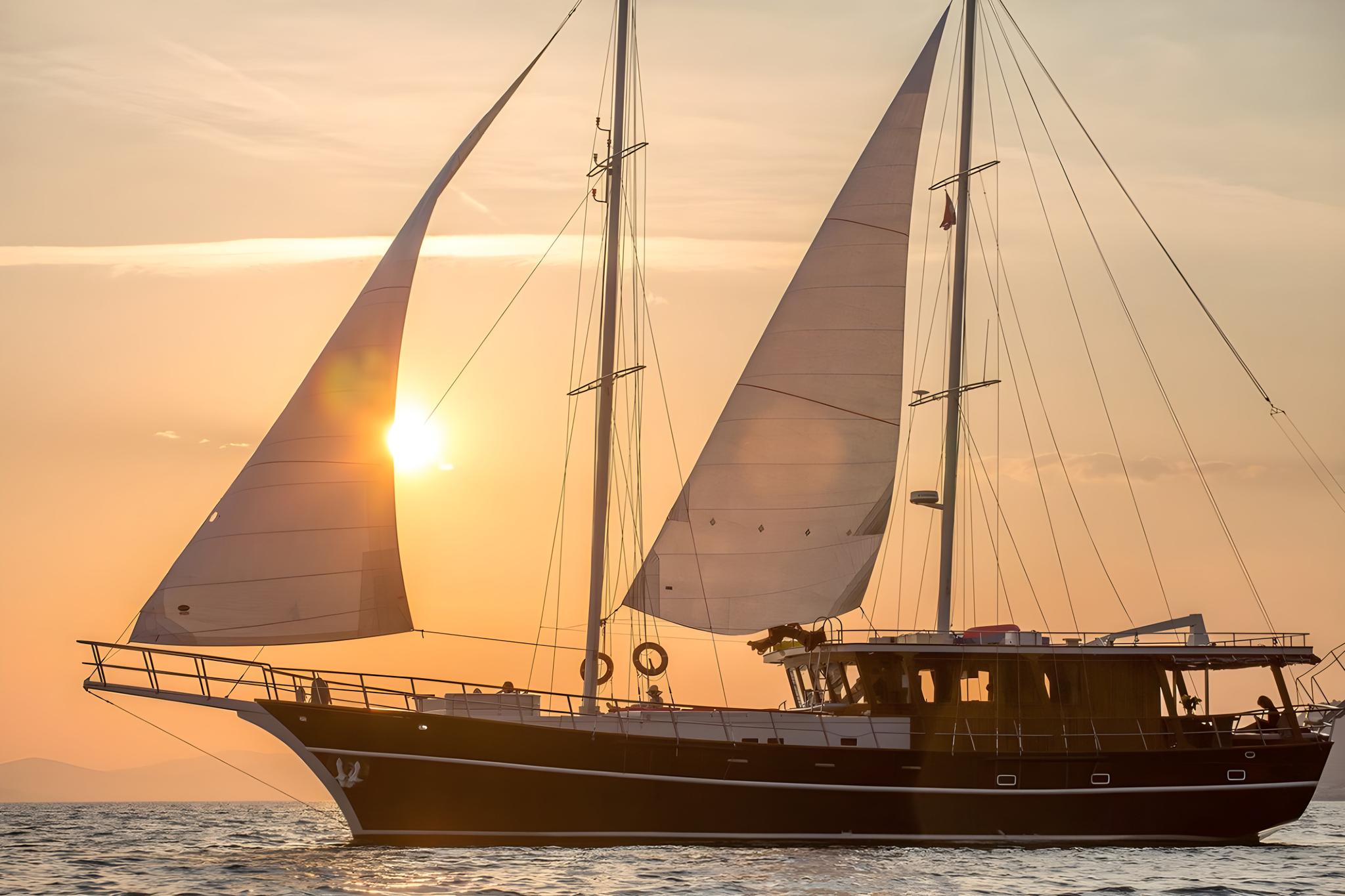 Traditional wooden gulet with white sails deployed sailing at golden sunset
