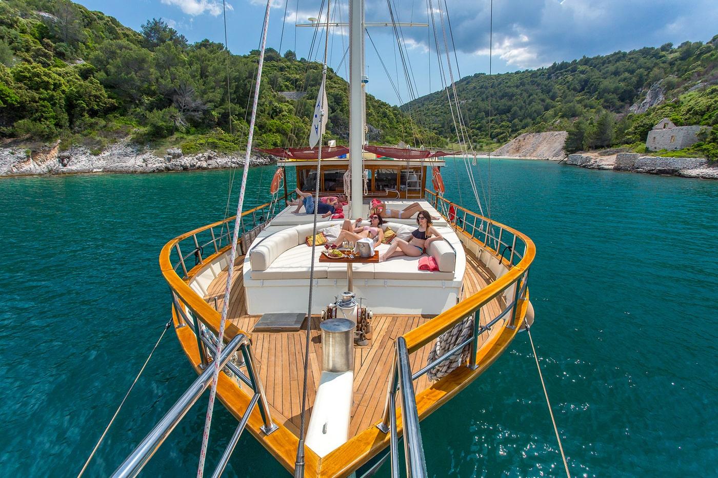 Traditional wooden gulet yacht bow deck with guests relaxing in secluded Mediterranean cove