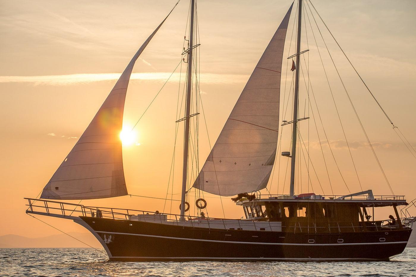 Traditional wooden gulet sailing yacht with white sails during golden hour sunset