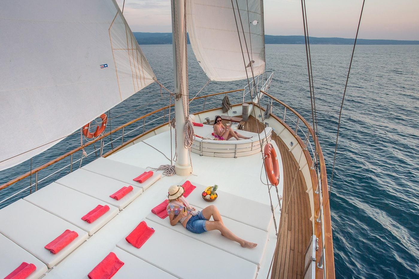 Gulet forward deck with guests sunbathing on white cushions with coral towels