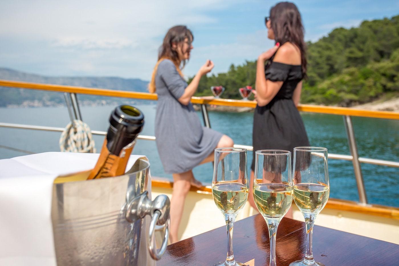 Three champagne glasses and ice bucket with guests socializing on luxury yacht deck