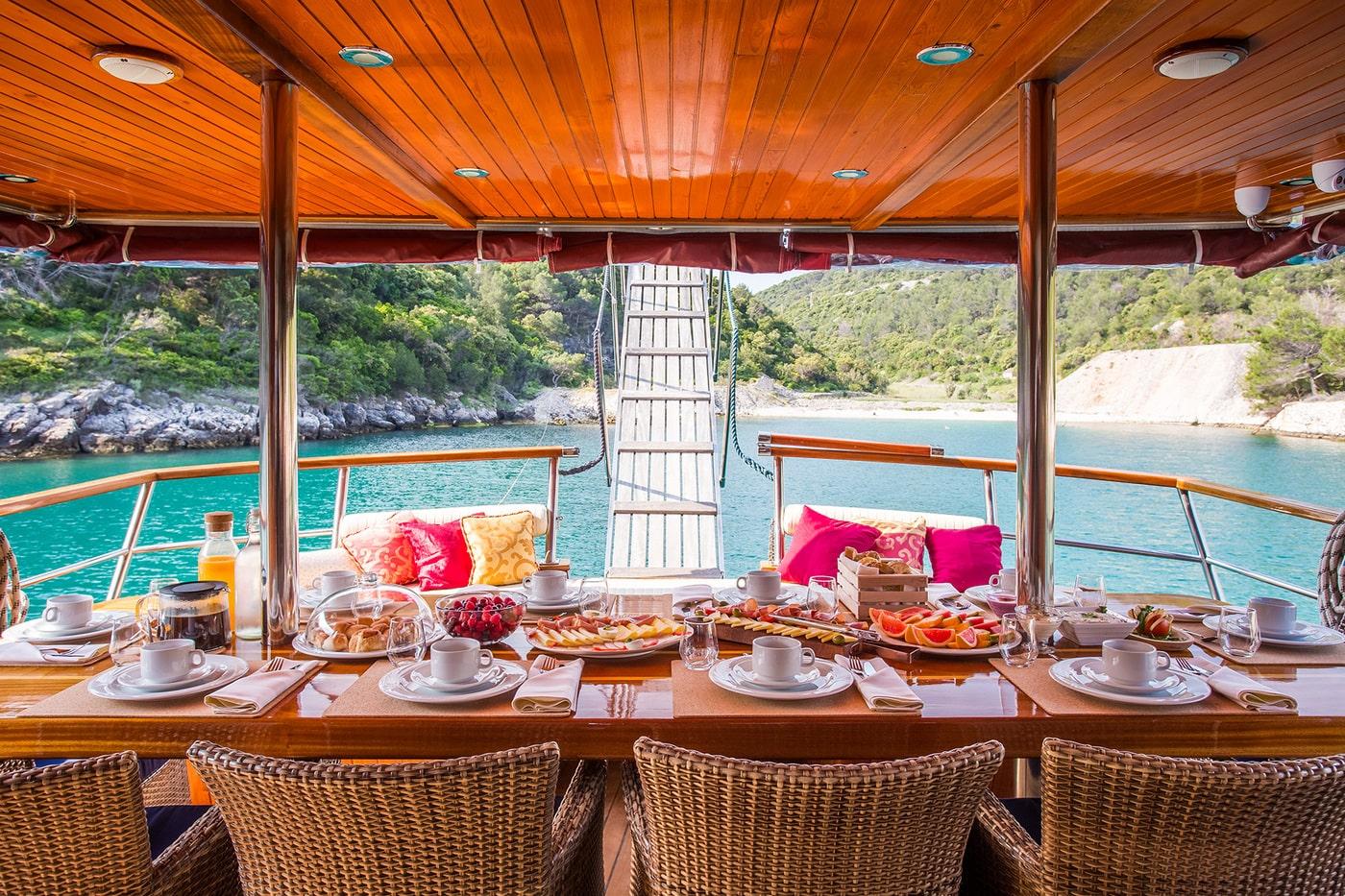 Elegant breakfast table setting on gulet aft deck overlooking turquoise bay