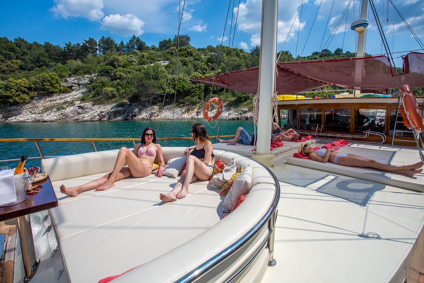 Two women sunbathing on white curved sunpad of traditional wooden gulet