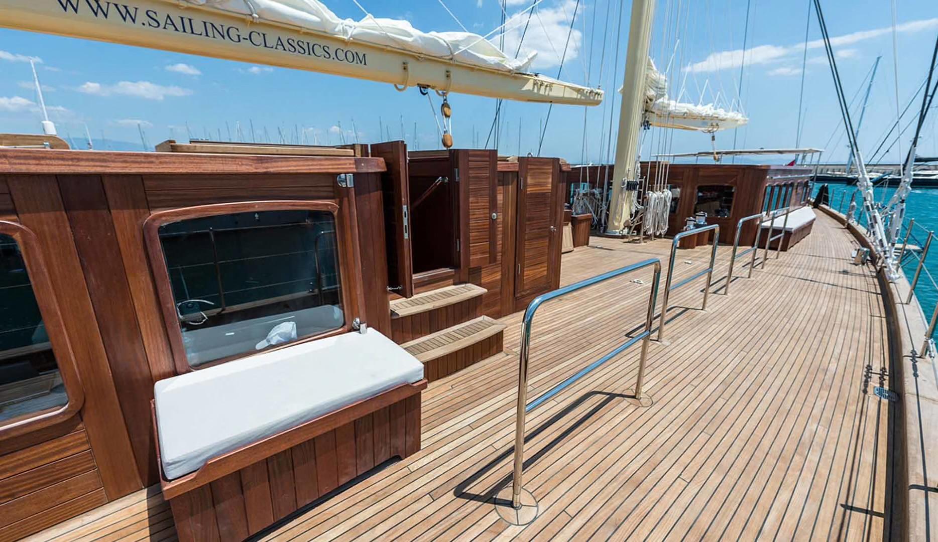 gulet main deck featuring teak planking, built-in wooden bench seating with white cushions, and stainless steel railings