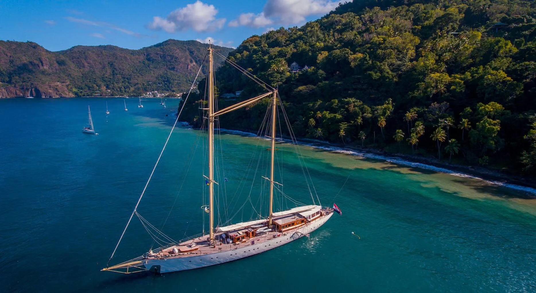 aerial view of traditional two-masted sailing yacht anchored in turquoise bay near forested coastline